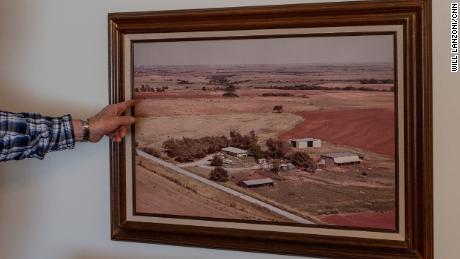 Terry Baker points to a photograph hanging on the wall of Cathy Baker&#39;s childhood home showing the family farm in the late 1900s.