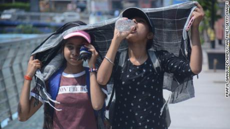 Girls cover their heads as they walk and drink water in the scorching afternoon heat in Mumbai.