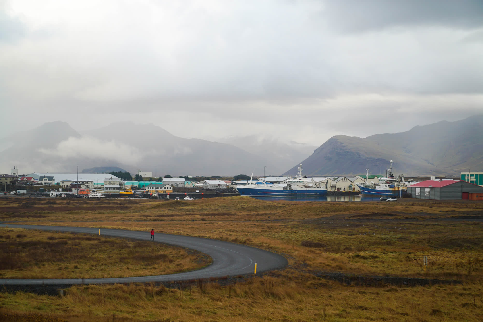 A foggy landscape with mountains in the distance and boats docked next to wooden houses