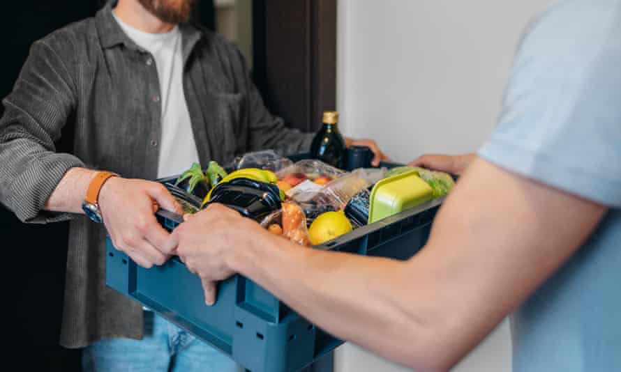 A man standing in front of the door and taking groceries delivered by a delivery man. Stay home, shop online