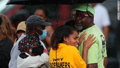 Bystanders gather under an umbrella as rain rolls in after a shooting at a supermarket on Saturday in Buffalo.