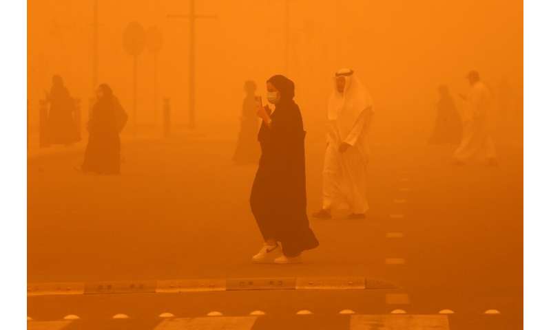 Pedestrians cross a road amidst a severe dust storm in Kuwait City