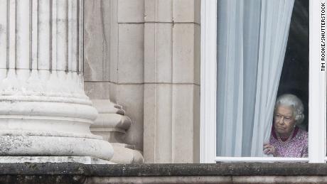 The monarch peers through the curtains of Buckingham Palace as she waits for the Patrons Lunch to start on the Mall in central London on June 12, 2016. 