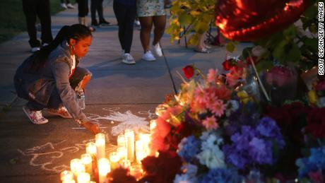 A woman chalks a message at a makeshift memorial outside of a Tops grocery store in Buffalo on May 15, 2022. 