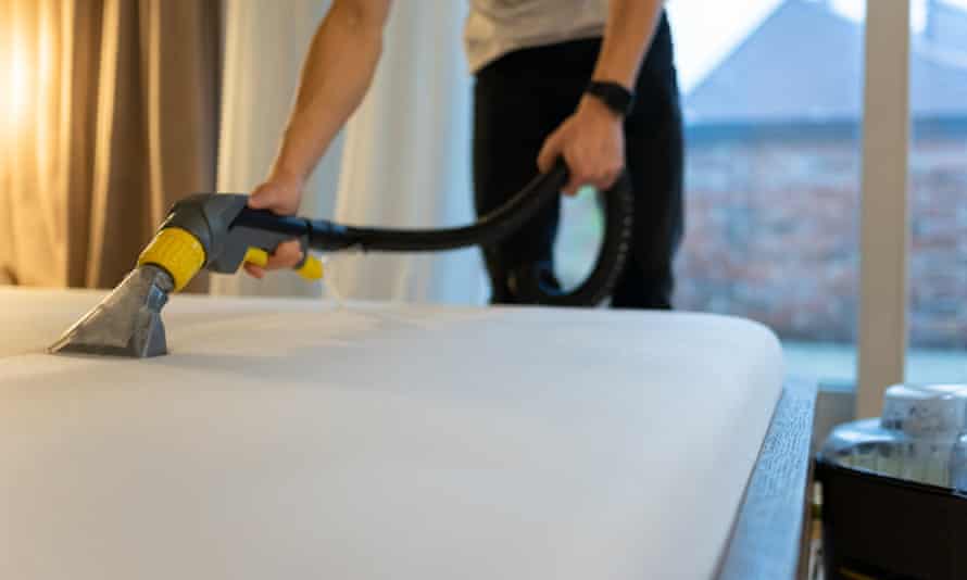 A person vacuuming a mattress