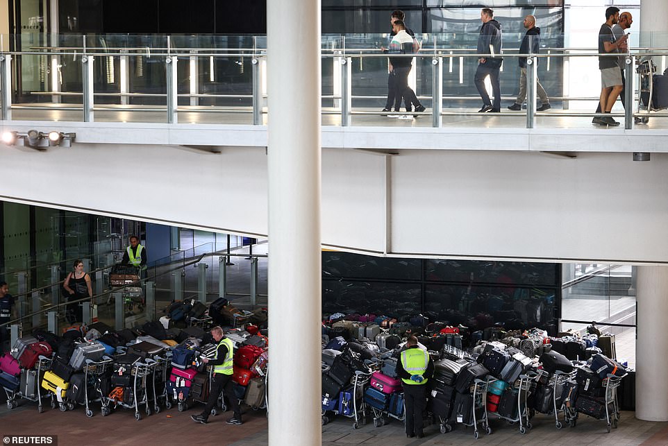 Airport workers stand next to lines of passenger luggage arranged outside Terminal 2 at Heathrow Airport in London