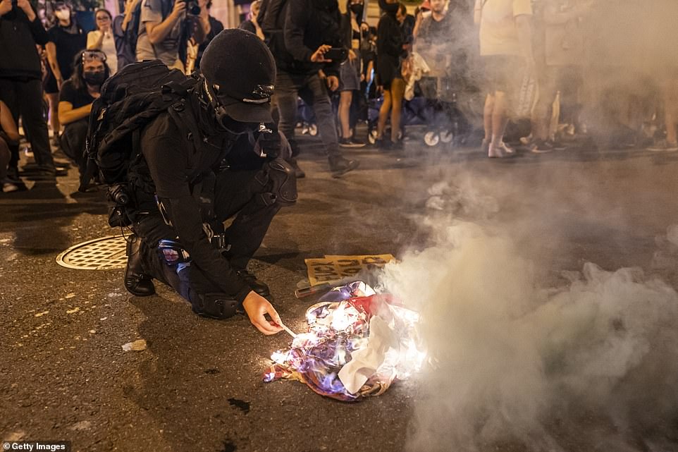 A protester lights a cigarette on a burning American Flag while marching with abortion-rights activists