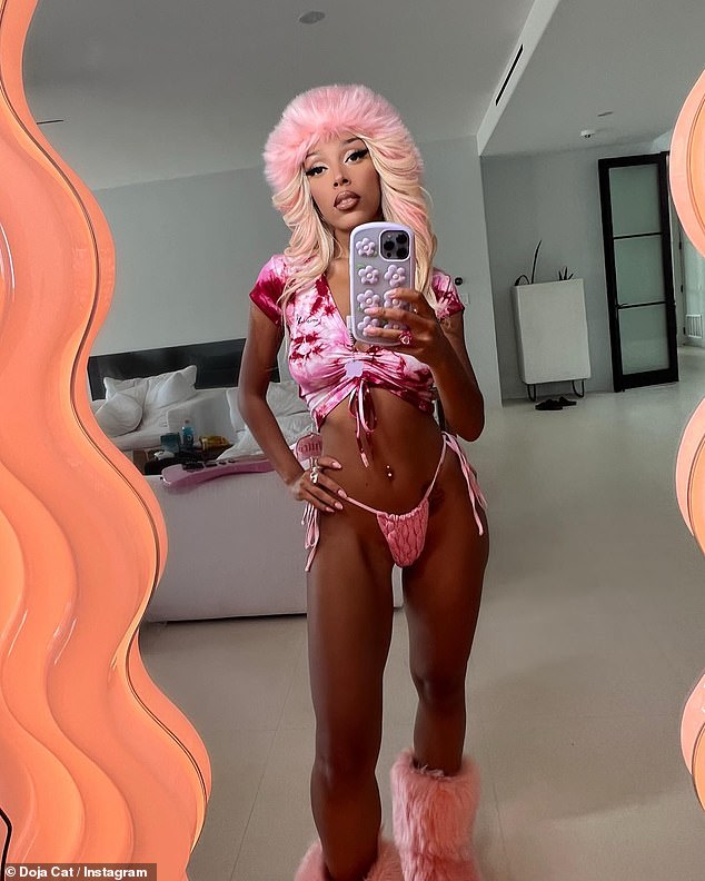 Doja Cat strips down into tie dye crop top and orange string bikini with matching wig and boots