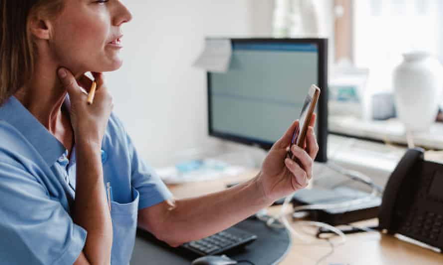 Female pediatrician using smart phone while explaining through video conference in officewoman checking throat while looking at mobile at desk