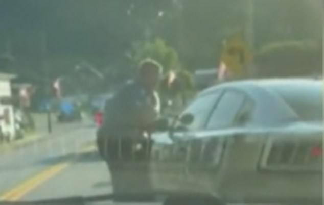 A police officer is seen taking cover behind a patrol car after shots were fired from the house