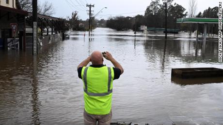 A local takes a photo of a road inundated by floodwaters in Camden in South Western Sydney, Sunday, July 3, 2022.