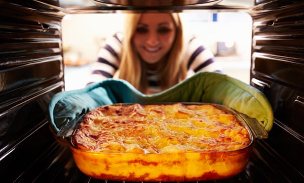 Woman takes dish of lasagne out of oven