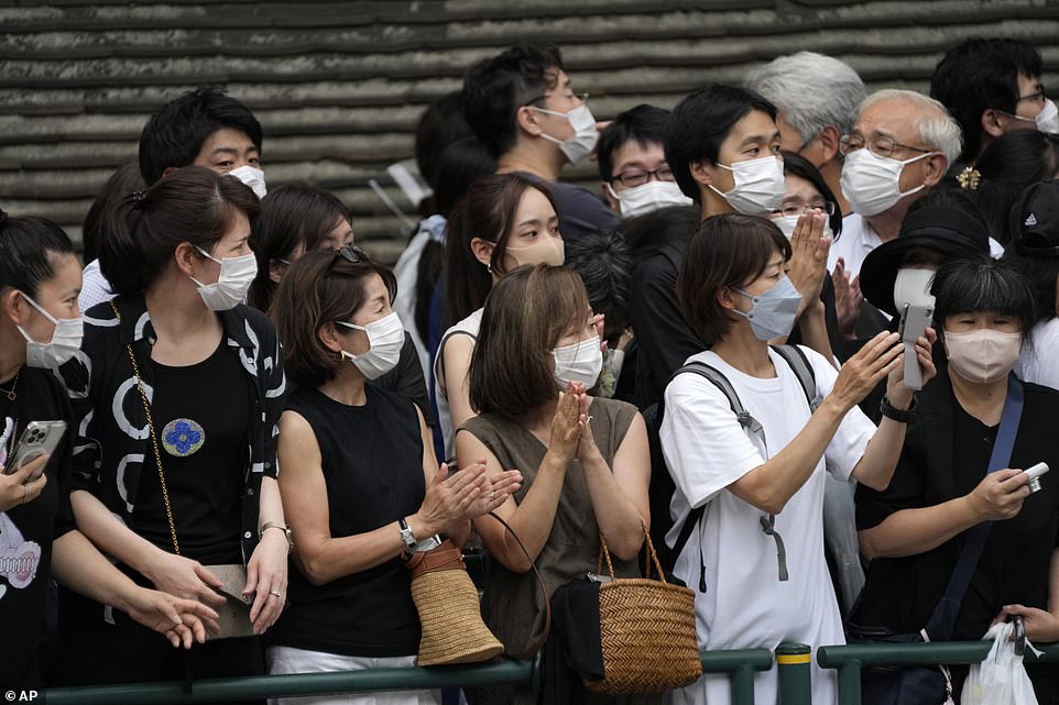 Some people take photos while others clasp their hands in prayer as the hearse carrying the body of Shinzo Abe passes