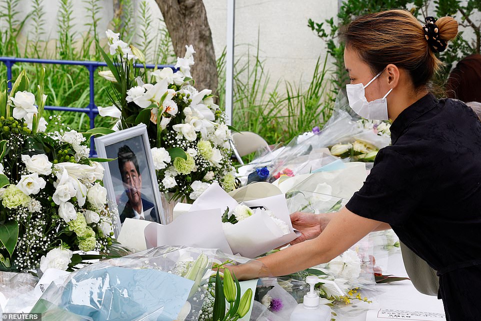 A woman offers flowers as people mourn for late former Japanese Prime Minister Shinzo Abe at the Headquarters of the Liberal Democratic Party in Tokyo