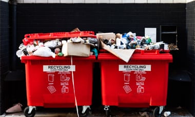 Red recycling bins overflowing with rubbish on the street.