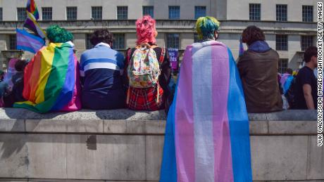 Protesters wrapped in pride and trans pride flags sit on a wall during a trans rights demonstration outside Downing Street. 