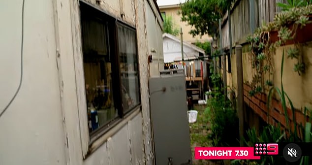 Paint is seen peeling on the outside of the home as a sideway leads to a backyard full of junk