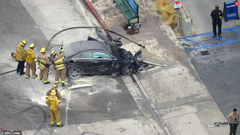 Fire department officials are seen on Thursday with a burnt-out car following the crash