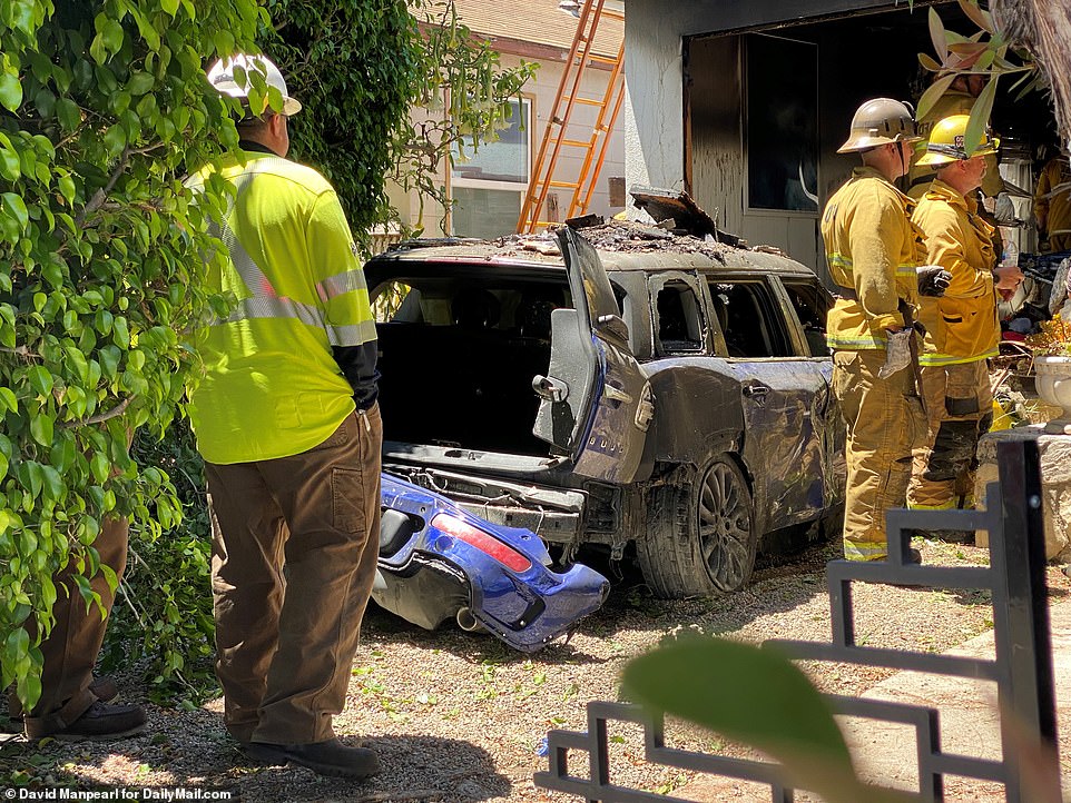 Firefighters survey the scene with Heche's wrecked car in the middle of the picture