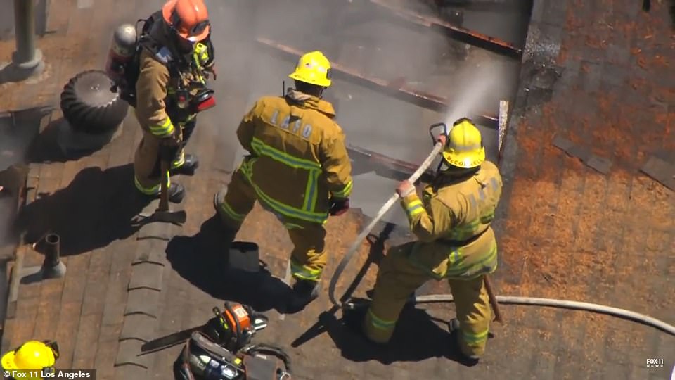 Firefighters dampen down the remains of the blaze as they stand on the rooftop of the home