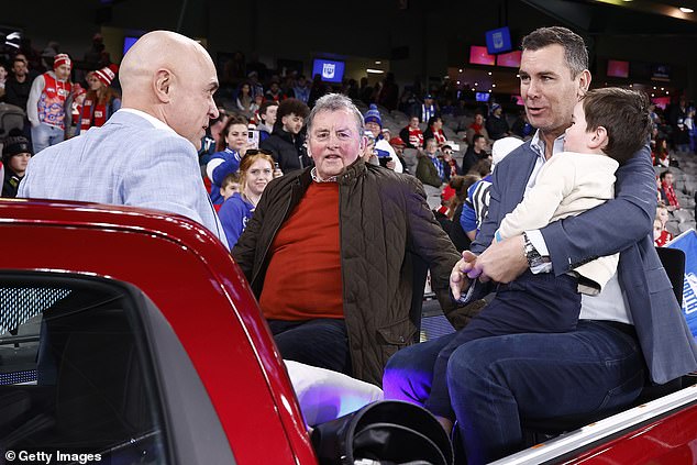 The 51-year-old was spotted cradling his son in his lap as watched the game between North Melbourne Kangaroos and the Sydney Swans