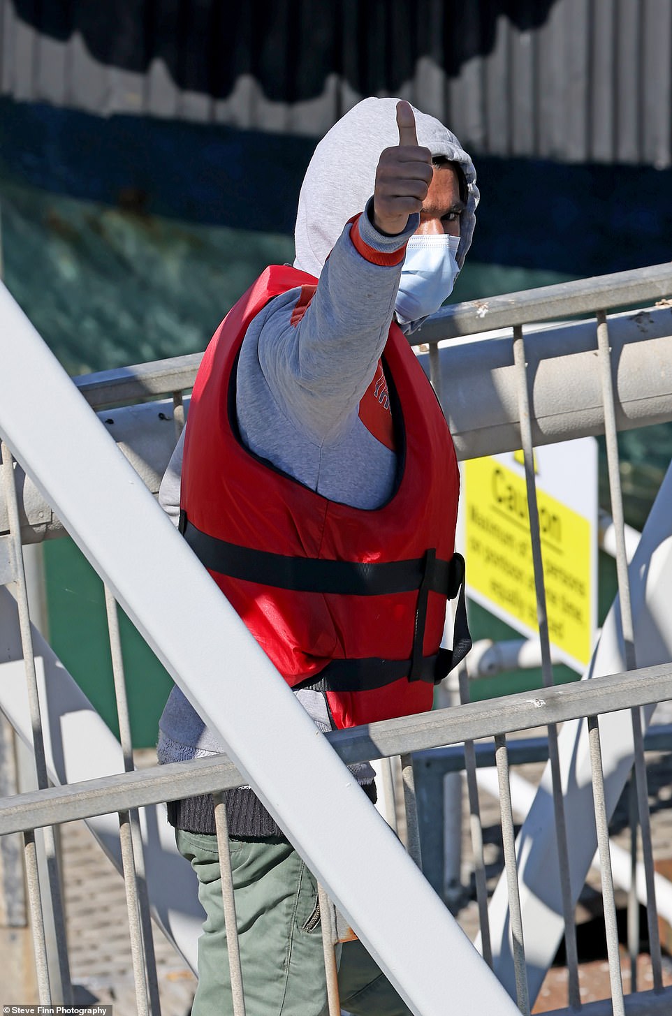 A migrants gives a thumbs up as he is escorted ashore by Border Force officials this afternoon to be loaded onto a coach and processed