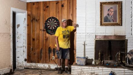 Sam Quillen poses for a portrait next to a painting of his father at his damaged property, which was a dentist&#39;s office as well as residential housing.