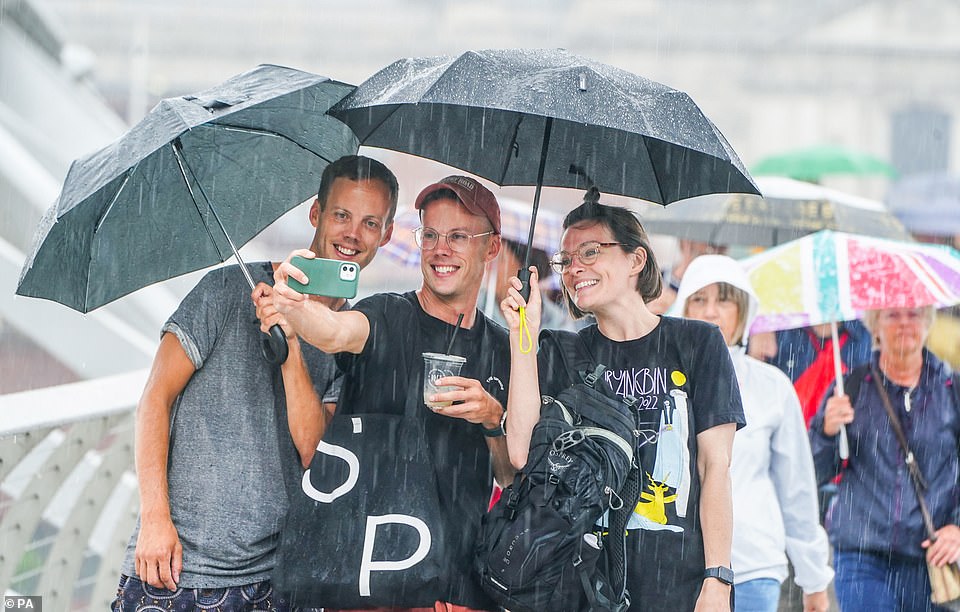 Three people take a selfie under umbrellas as they stand on Millennium Bridge in London during heavy rain on Tuesday afternoon