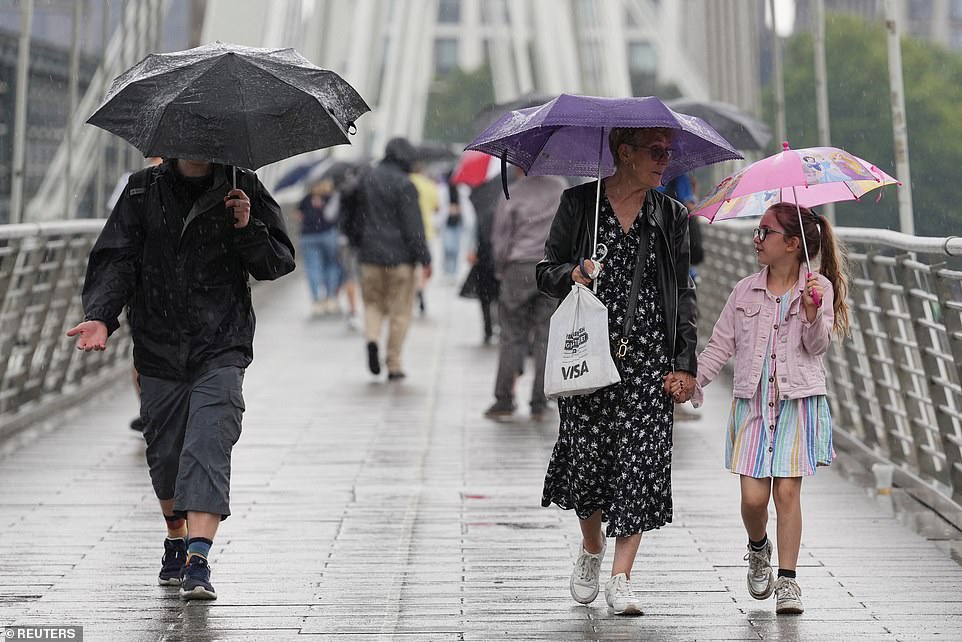 People hold umbrellas during a downpour of rain in central London this afternoon