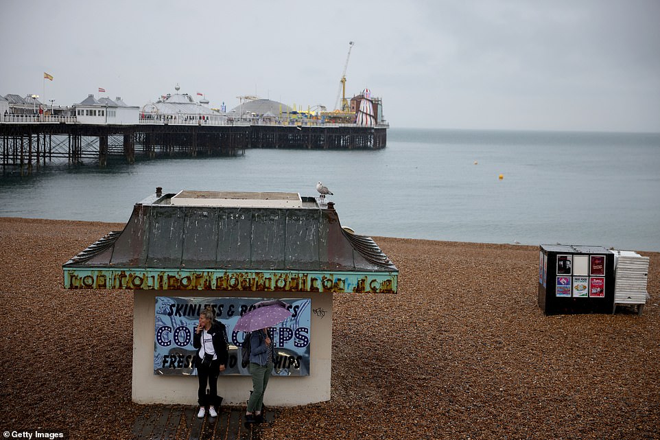 Two women seeks shelter on Brighton seafront after rain breaks out on Monday