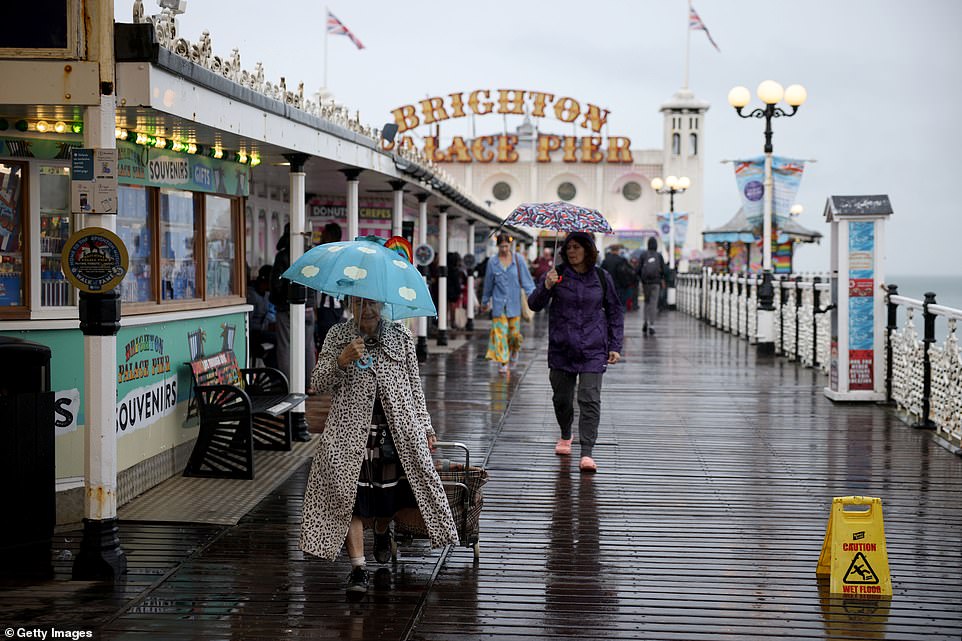 People open their umbrellas while strolling along Brighton Pier during a downpour on Monday