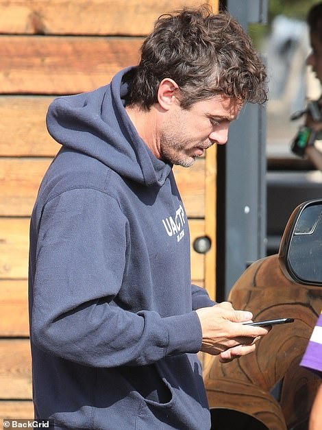 Casey Affleck taking a look at his phone as he picks up a cup of coffee in Los Angeles this morning, the same day his brother is due to marry across the country in Georgia