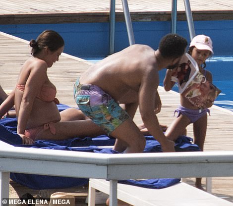 Out of the sun: The youngster had her head protected by a baby pink baseball cap as she leaned on her mum's sun lounger