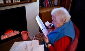 Energy Bills Elderly senior independent 99 year old lady at home in front of fire using a magnifier to read her latest household energy bills<br>DJ3BA4 Energy Bills Elderly senior independent 99 year old lady at home in front of fire using a magnifier to read her latest household energy bills