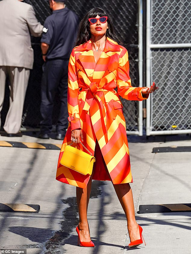 Jameela Jamil cuts a stylish figure in a vibrant striped trench coat and scarlet heels