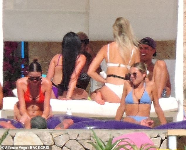 In the foreground, more women relax by the pool, topping up their tans while speaking to a male contestant