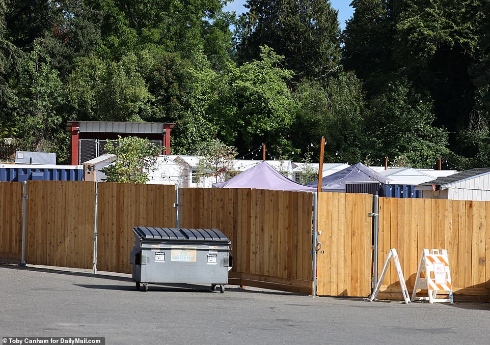 Tops of the structures are just barely seen over the wooden fence in place as a barrier between the village and neighborhood