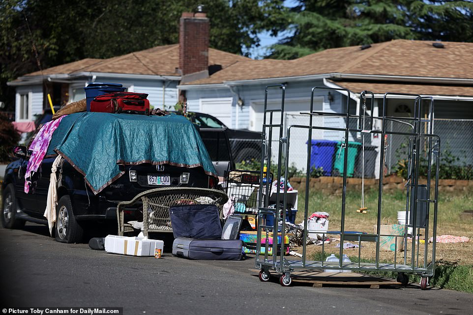 Parked vehicles covered with tarps are seen along North Syracuse Street near Peninsula Crossing Trail. Belongings are trash is strewn on the pavement and in the yard of someone's private residence