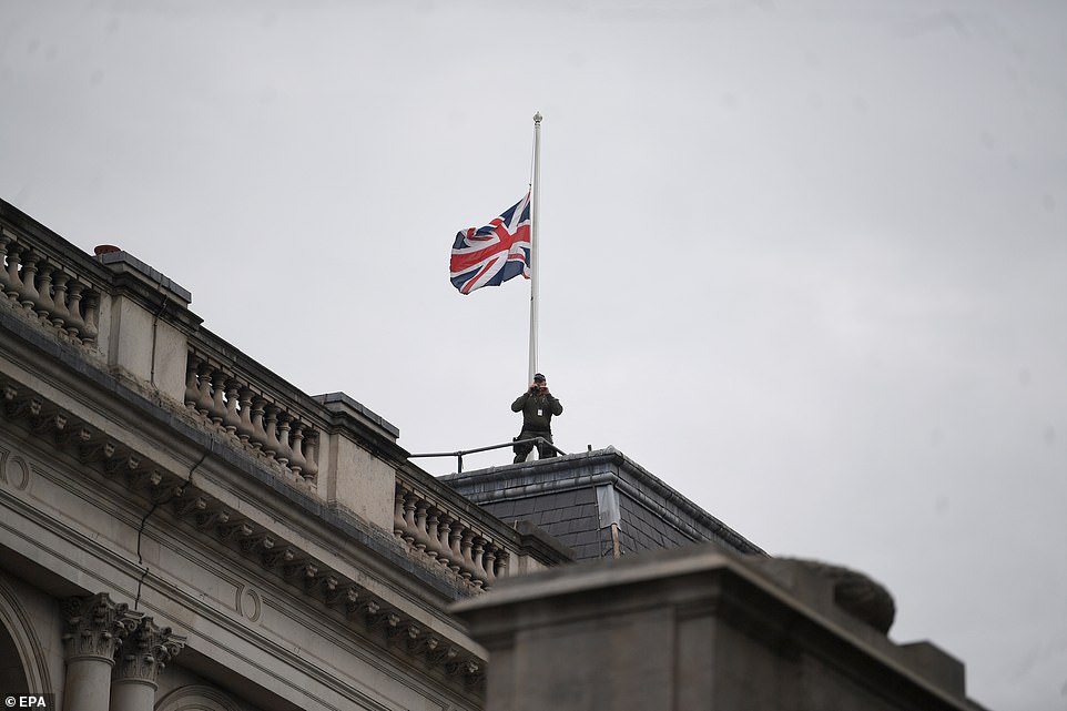 Below the Union Flag at half mast, a police spotter surveys the crowd atop Buckingham Palace this morning