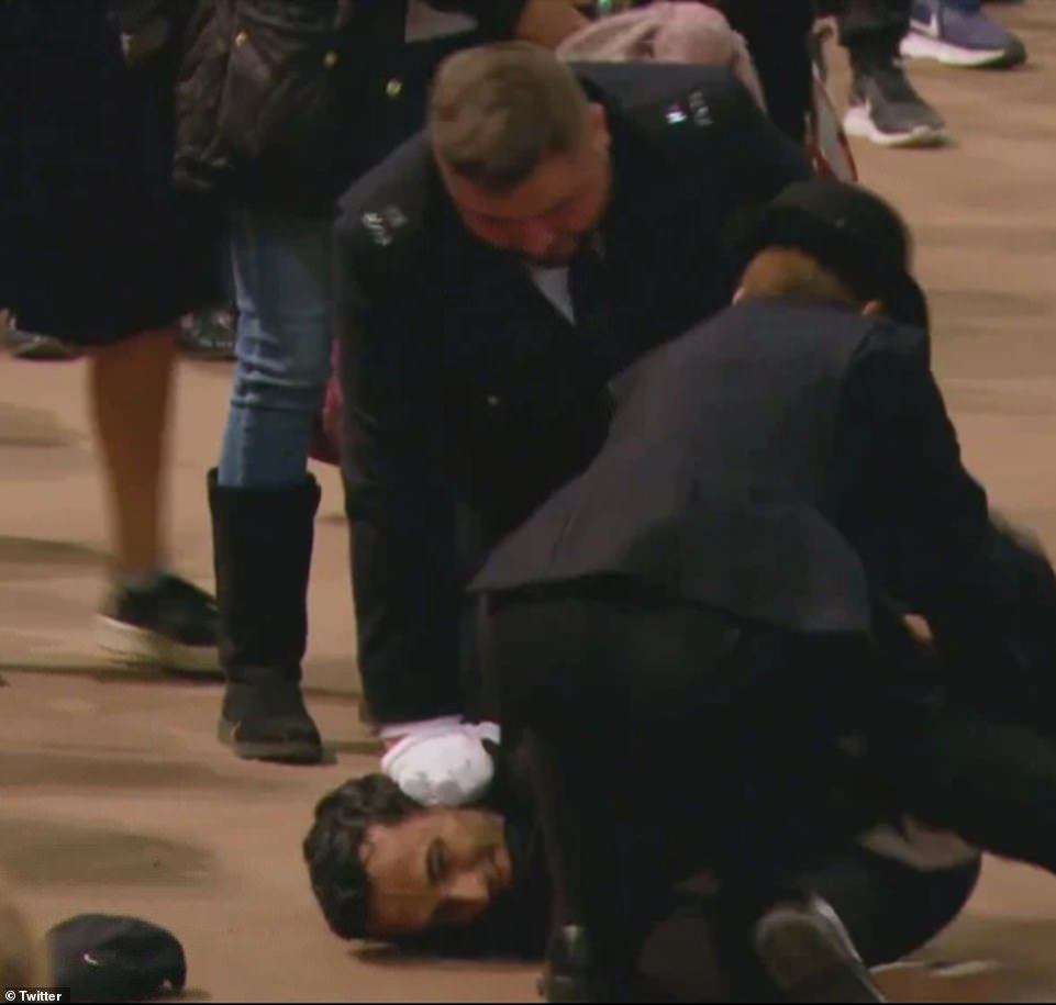 The man who grabbed the Standard smirks as he is held to the floor by police who had dragged him away from the coffin