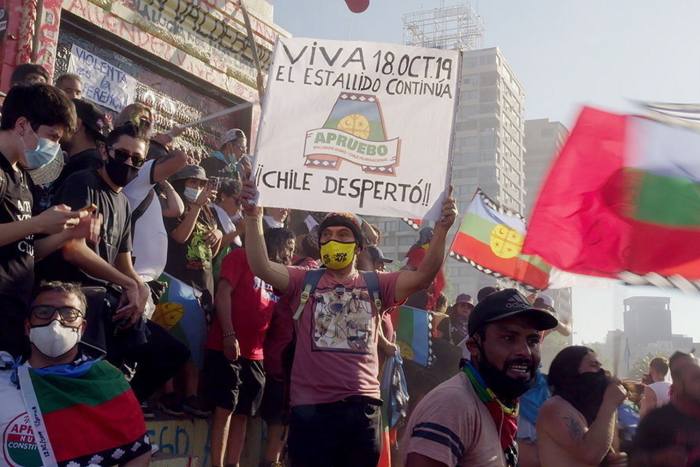 A group of protesters wearing medical masks and holding up flags and a sign that says ‘Chile Desperto’