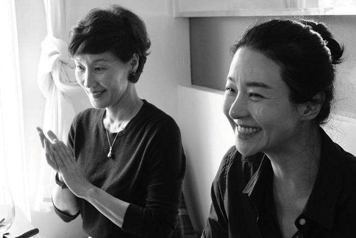 A black and white still of two women sitting together, smiling