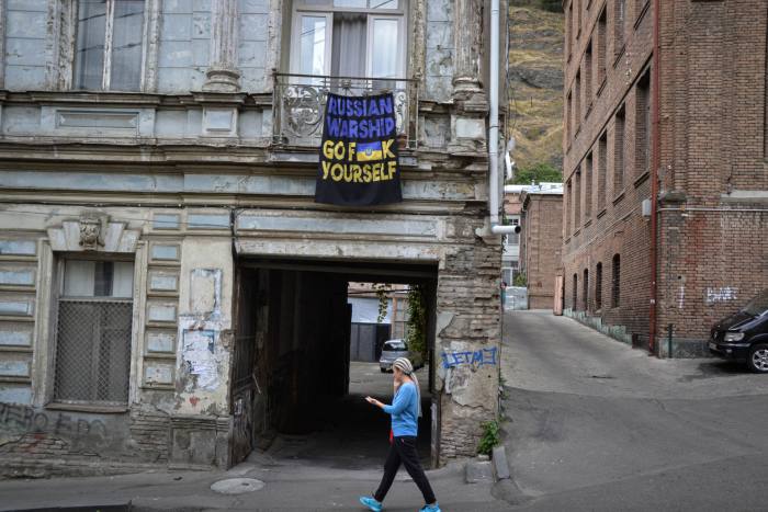 A young woman walks past a building where a banner in blue and yellow hangs from a balcony