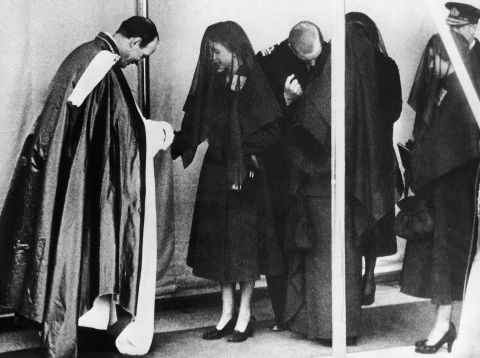 Queen Elizabeth II shakes hands with the Dean of Windsor, the Rt. Rev. Eric Knightley Chetwode Hamilton, after the funeral service. Behind the Queen her husband, Prince Philip, bends down as he talks with the Queen Mother.