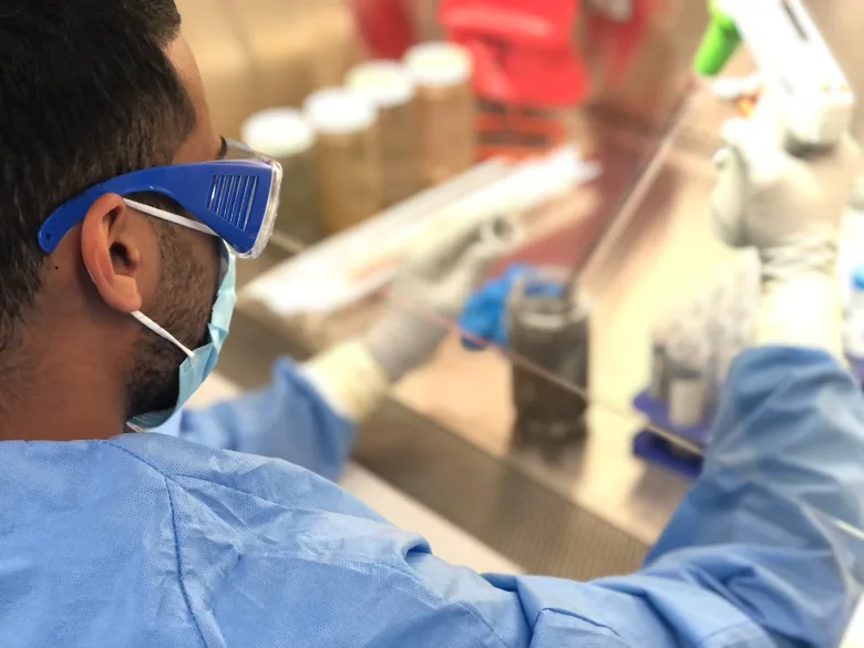 A researcher in scrubs operates equipment.