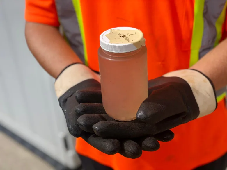 Two hands hold up a jar with brown liquid in it.