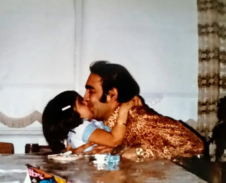 A man dressed in 70s fashion kisses a young girl.