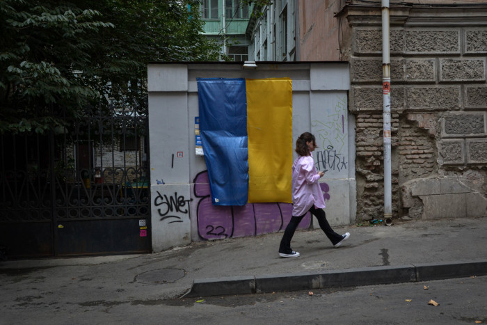 A young woman walks past a Ukrainian flag draped over a wall