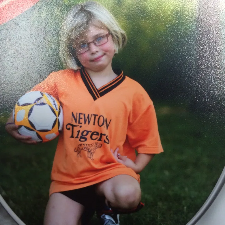 A girl holds a soccer ball and kneels on the grass. 