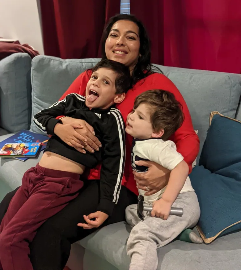 A smiling woman hugs her two children who are making goofy expressions.